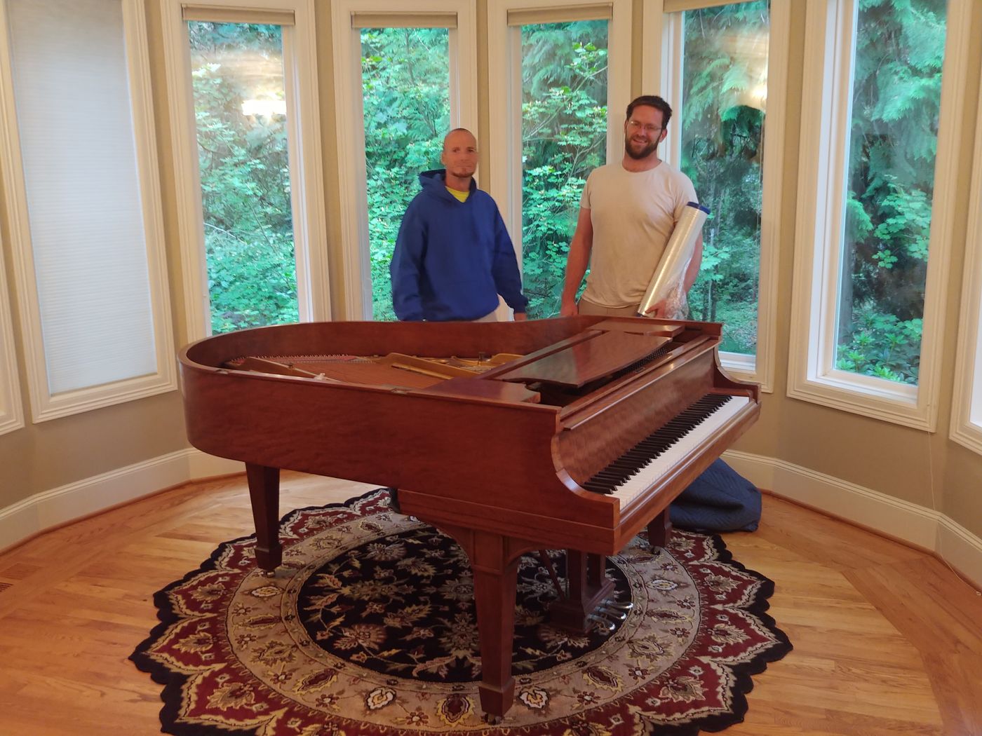 Two movers beside a grand piano in a round sunroom